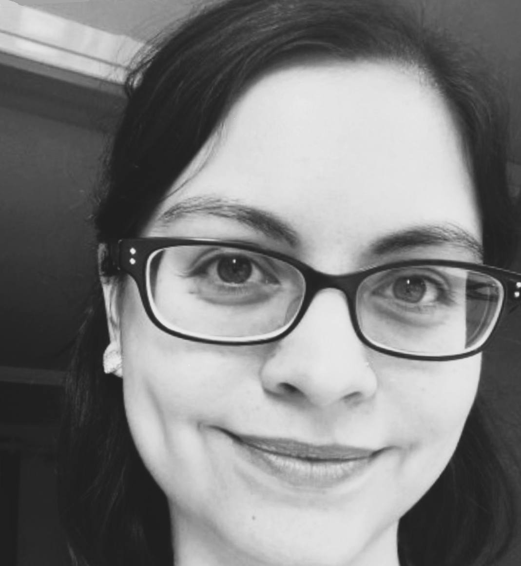 A close-up, black-and-white portrait of a woman with dark hair and glasses, smiling softly at the camera.