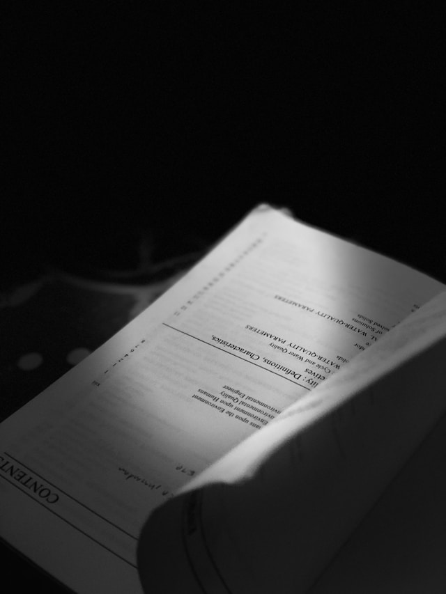 A partially opened book with pages displaying text, set against a dark background.